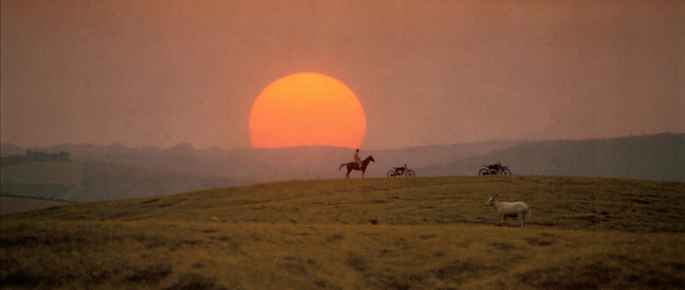 Lone rider on horseback on a ridgeline at dusk, dirt bikes parked, a white buck watching, a huge sun setting